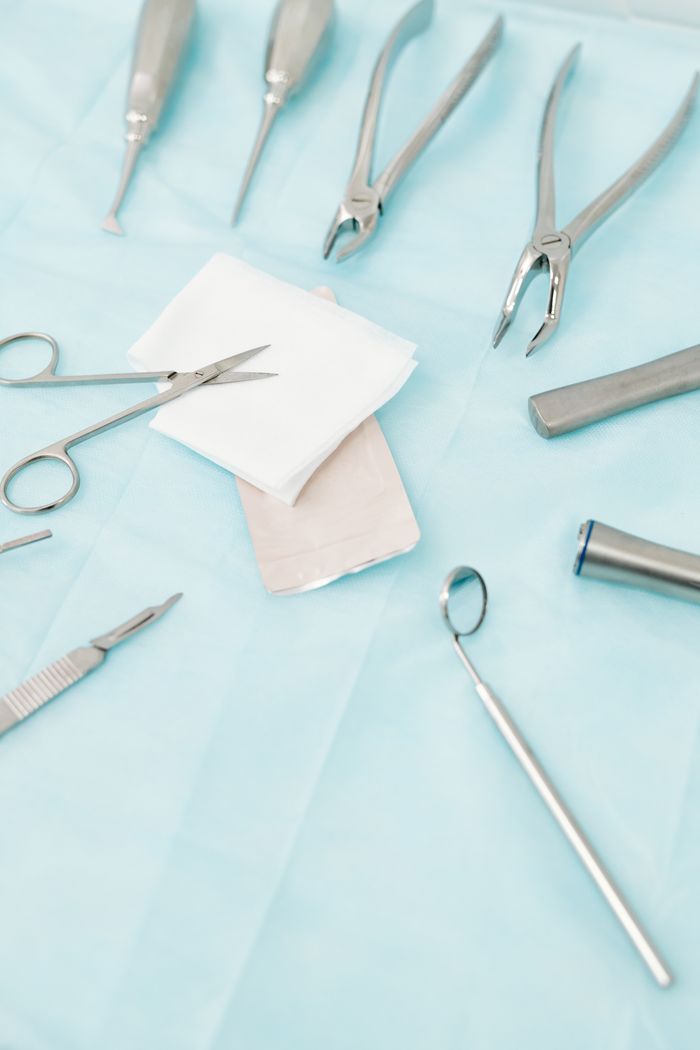 who-we-are A close-up view of various stainless steel dental instruments arranged on a sterile blue background.